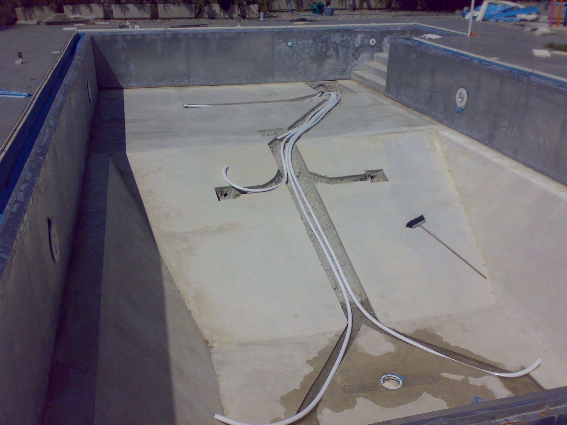 Piscina vuota in cemento in costruzione, tubi bianchi visibili all'interno.
