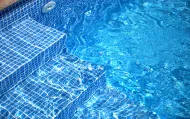 Gradini della piscina rivestiti di piastrelle blu immersi in acqua limpida con increspature in superficie.