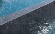 Bordo di una piscina piastrellata scura con acqua che trabocca nella piscina principale.