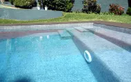 Piscina con gradini integrati, acqua cristallina e azzurra, circondata da pietra grigia e verde.