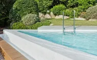 Piscina con acqua limpida, circondata da cemento bianco e verde.