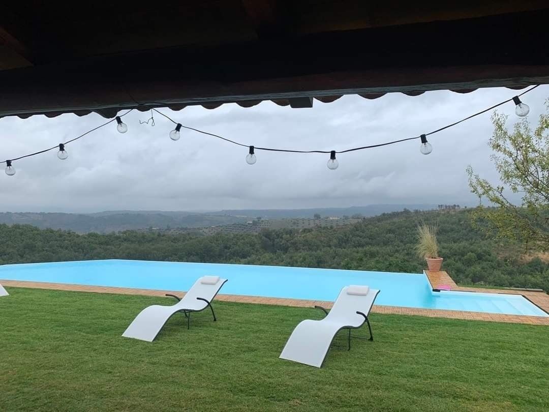 Due sedie a sdraio bianche sull'erba verde accanto a una piscina a sfioro, con vista sulla foresta sullo sfondo.