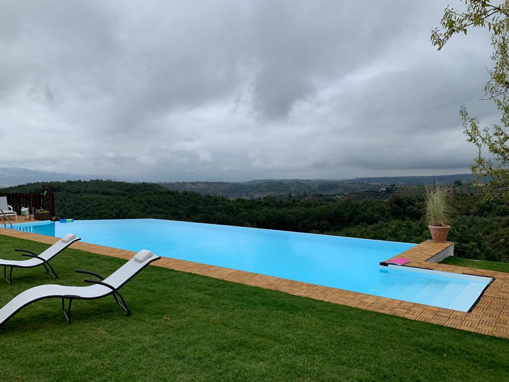 Piscina a sfioro con vista su un paesaggio verdeggiante e alberato.