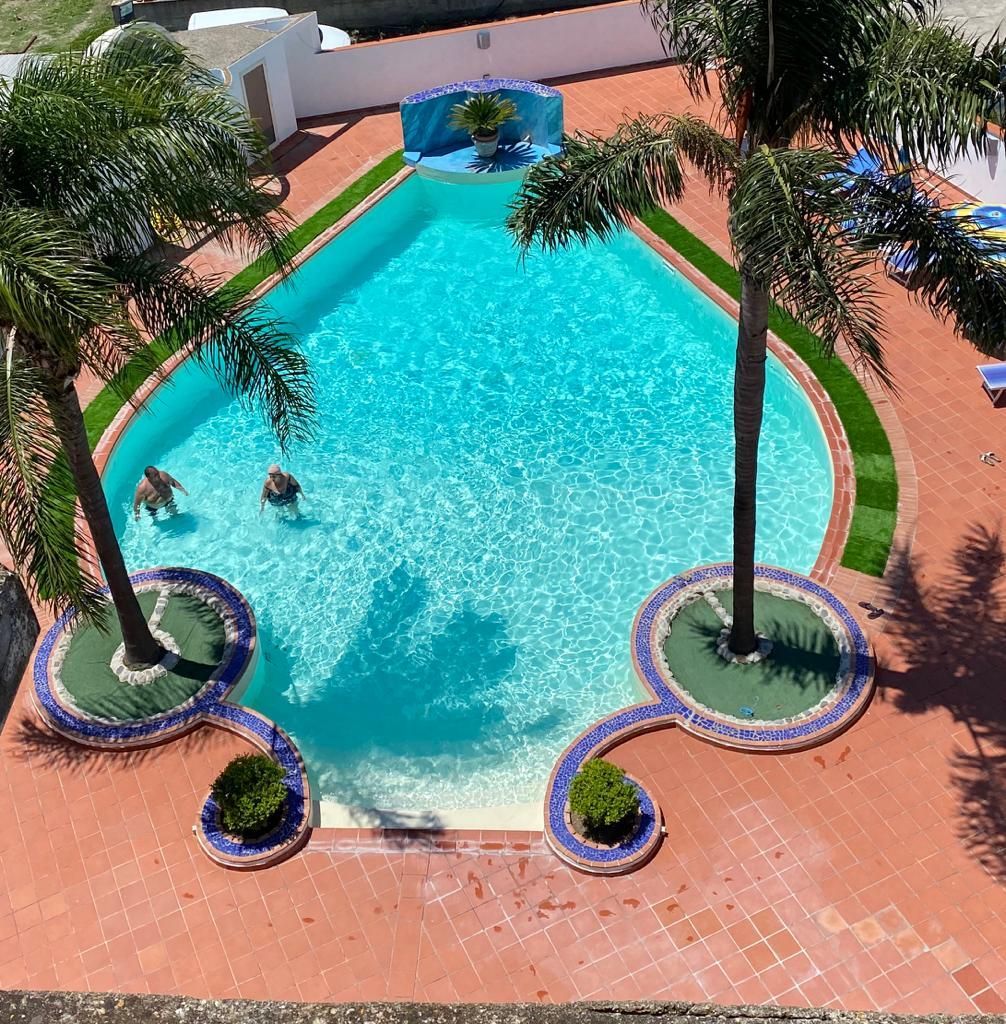 Piscina con palme, patio in mattoni rossi e due persone che nuotano.