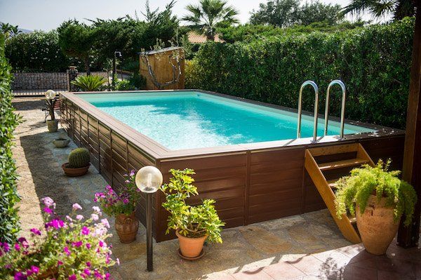 Piscina rettangolare fuori terra circondata da pannelli in legno, gradini e piante.