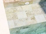 Piscina rivestita in pietra con acqua limpida che riflette la luce, lampada sospesa. Tonalità beige e bianco sporco.