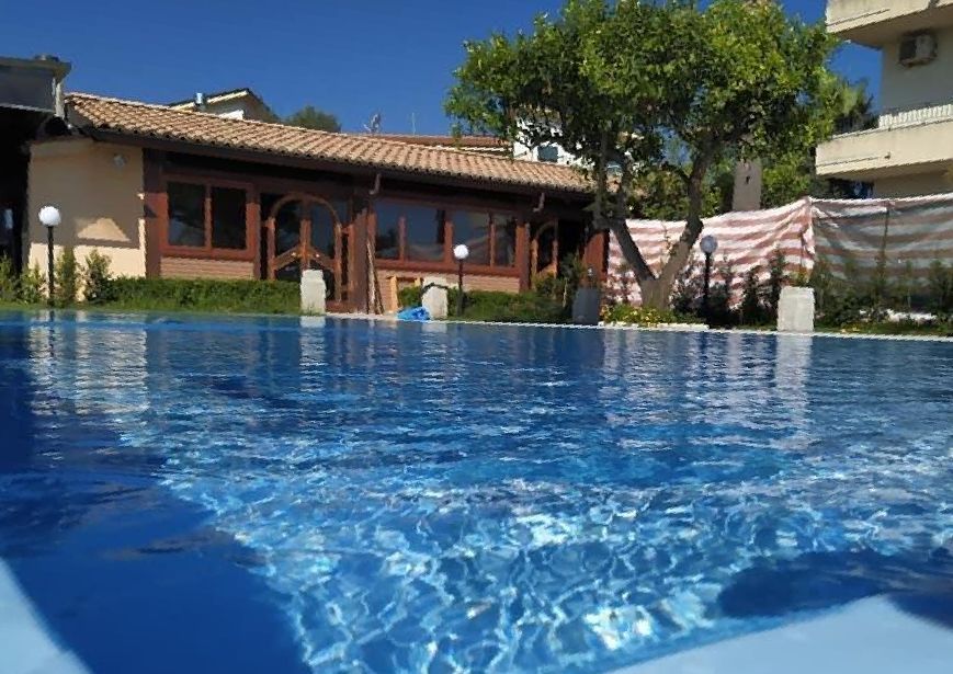 Piscina di acqua blu in cui si riflette un edificio con struttura in legno e tetto di tegole; giornata di sole.