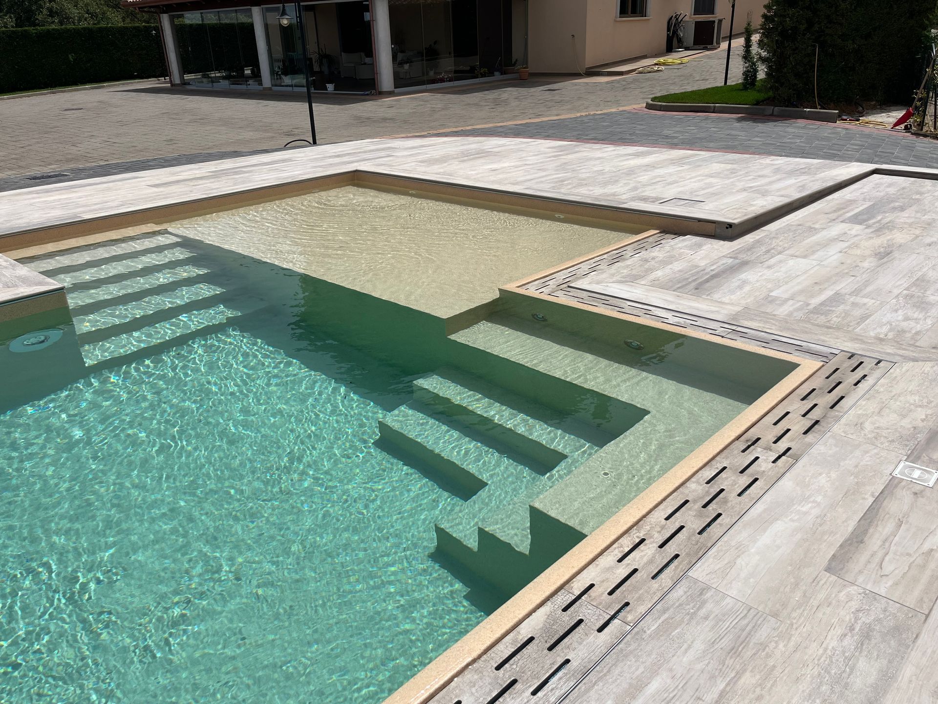 Piscina con gradini e pavimentazione in legno chiaro.