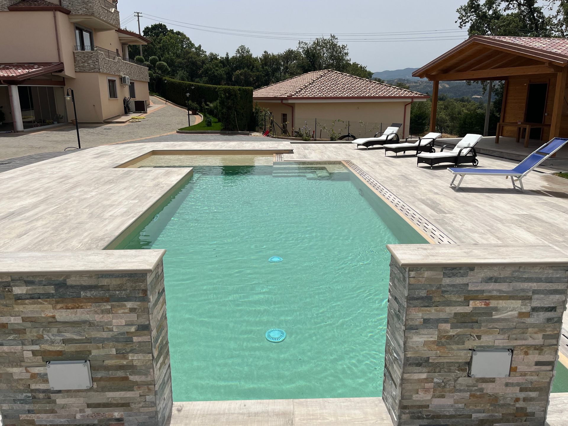 Piscina con acqua verde chiaro, dettagli in pietra e sedie a sdraio su un patio con vista.