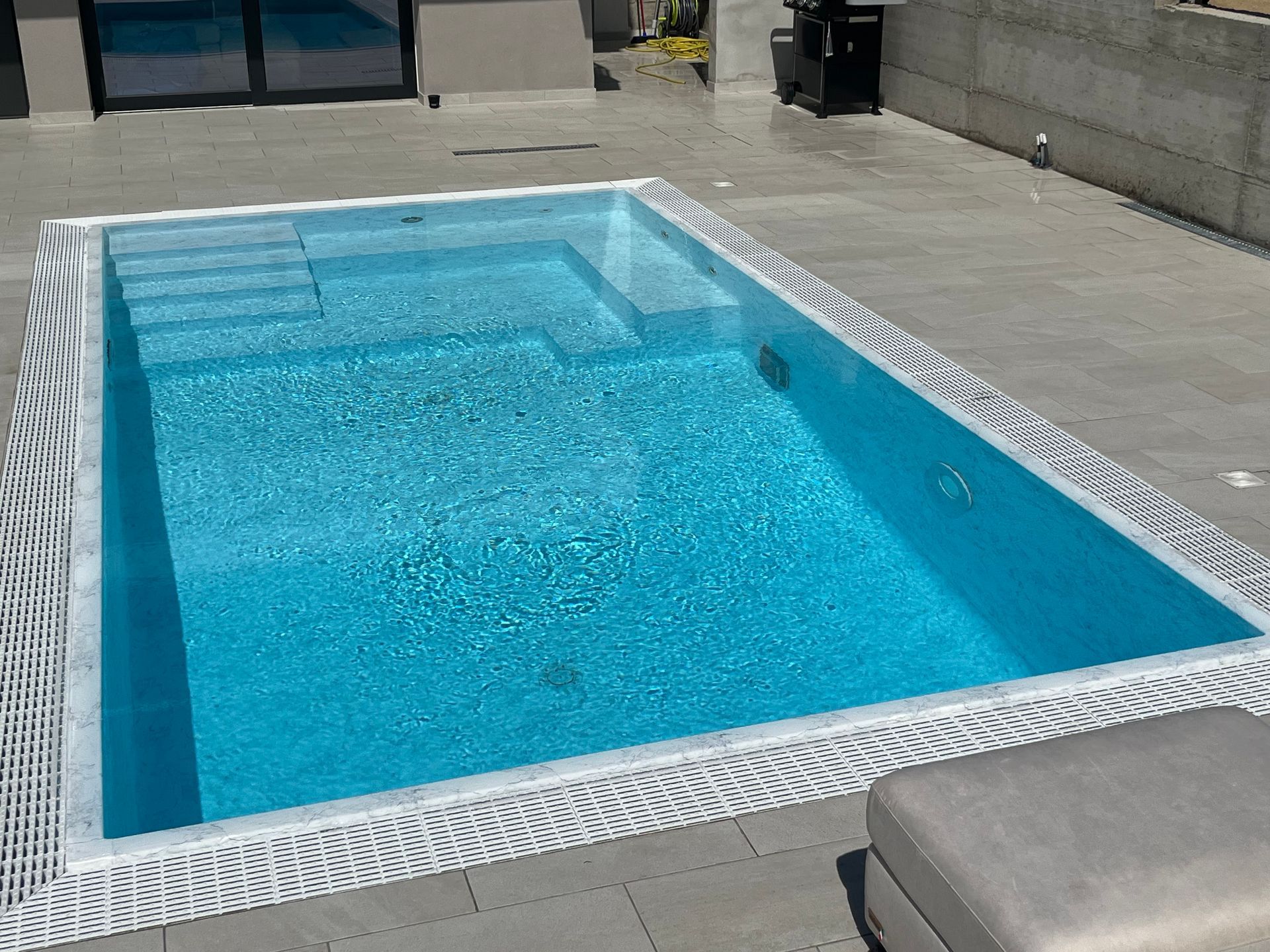 Piscina rettangolare con acqua turchese, gradini e bordo zebrato. All'esterno, su un patio in cemento.