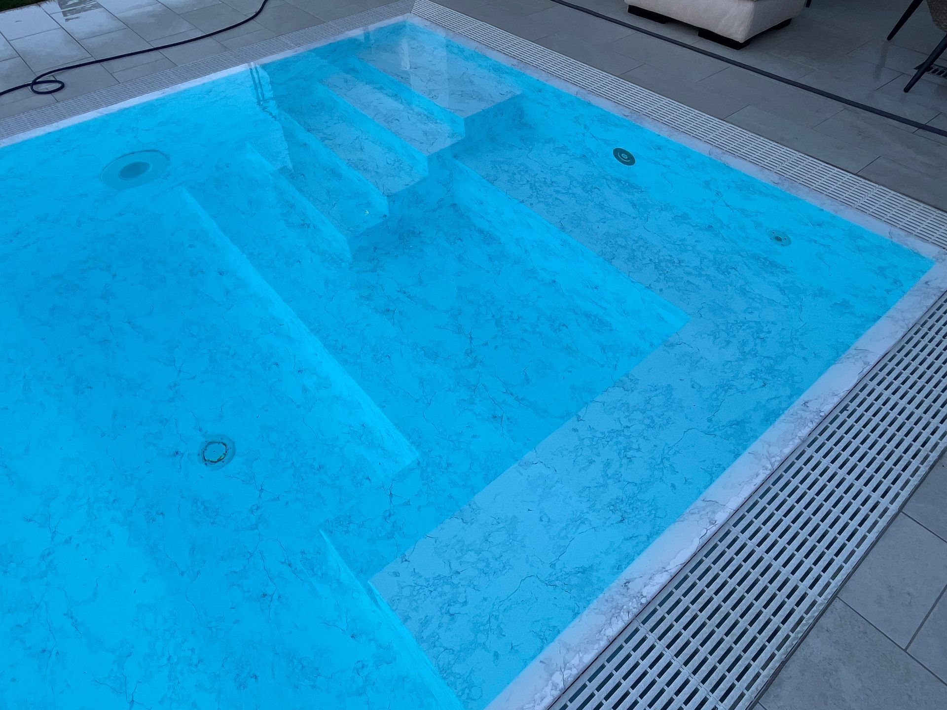 Piscina blu con gradini, patio in cemento e sistema di drenaggio dell'acqua.