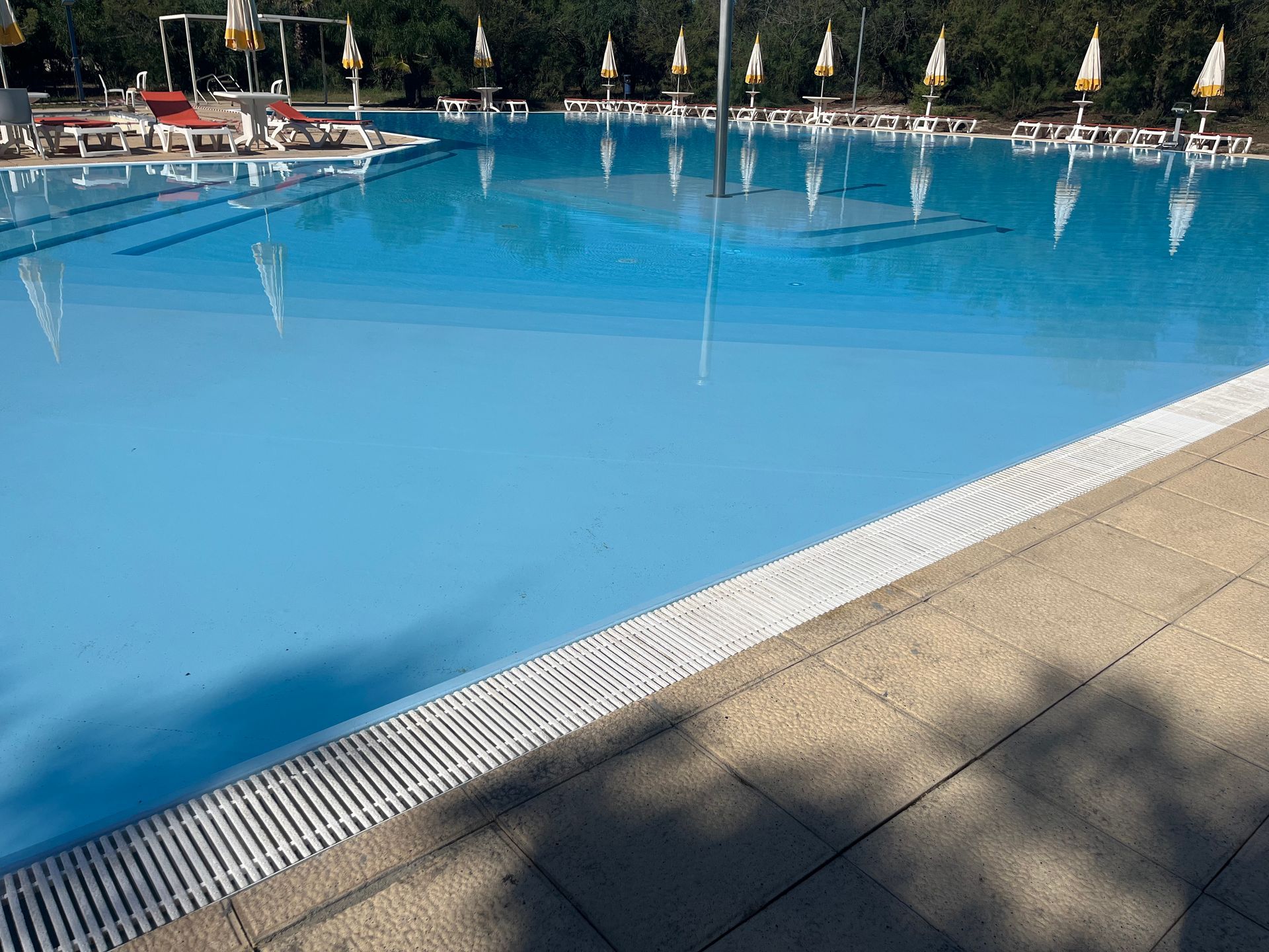 Una grande piscina di un azzurro brillante con bordi bianchi e un patio in cemento.