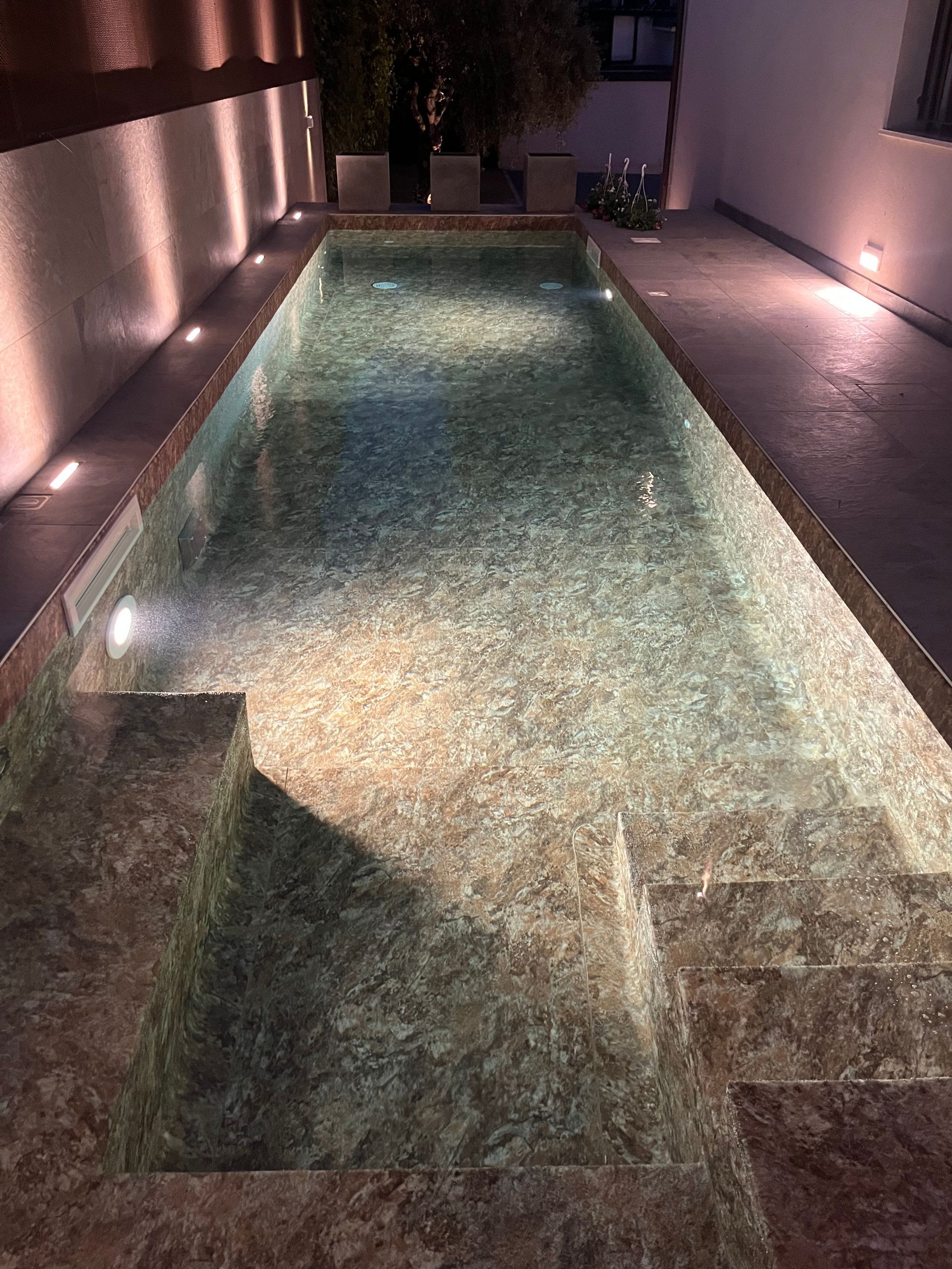 Piscina rettangolare illuminata di notte con gradini e illuminazione ambientale circostante.