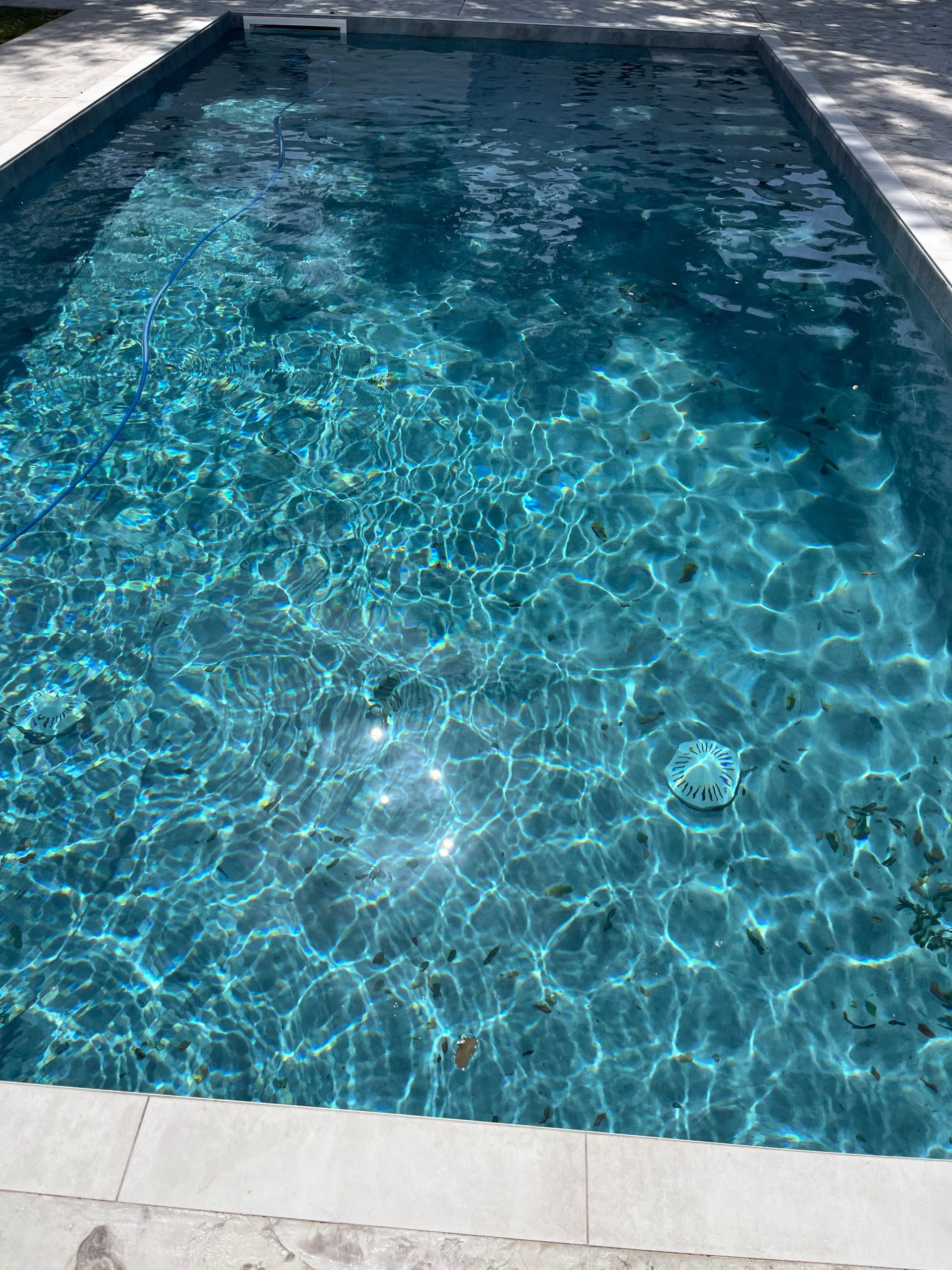 Una piscina rettangolare con acqua turchese, circondata da pietre chiare. La luce del sole si riflette sulla superficie.