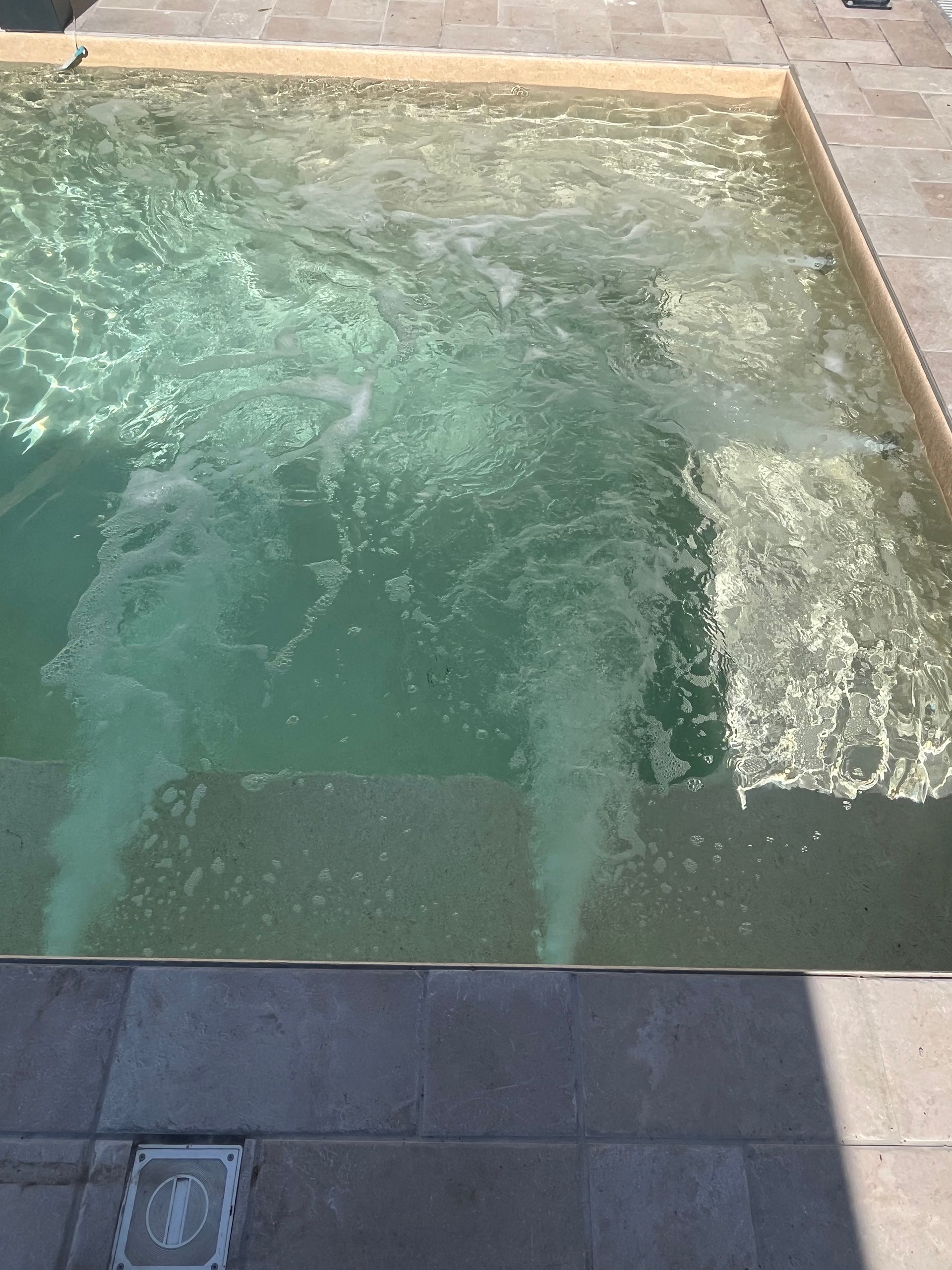Piscina con acqua gorgogliante, forse con getti d'acqua. Gradini visibili. Patio in pietra che la circonda.