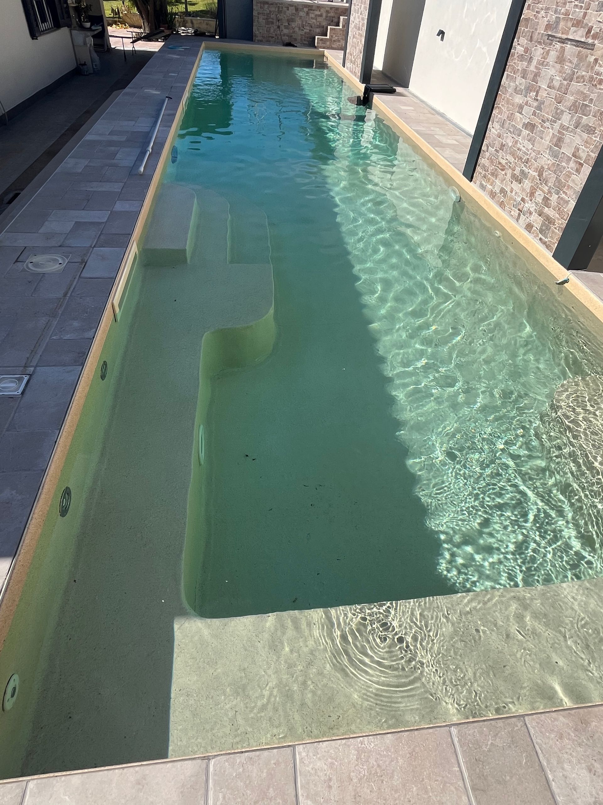 Piscina lunga e stretta con gradini e rivestimento in piastrelle chiare