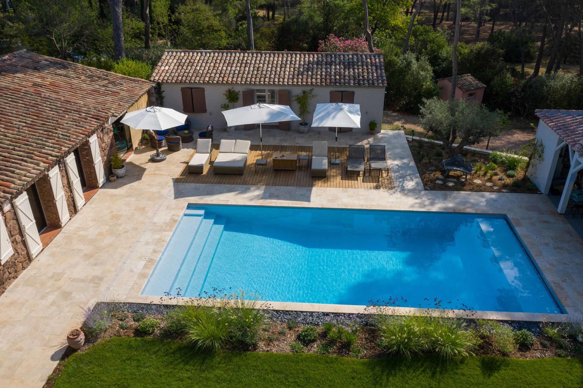 Piscina e patio con mobili da salotto, ombrelloni e un piccolo edificio con tetto di tegole.
