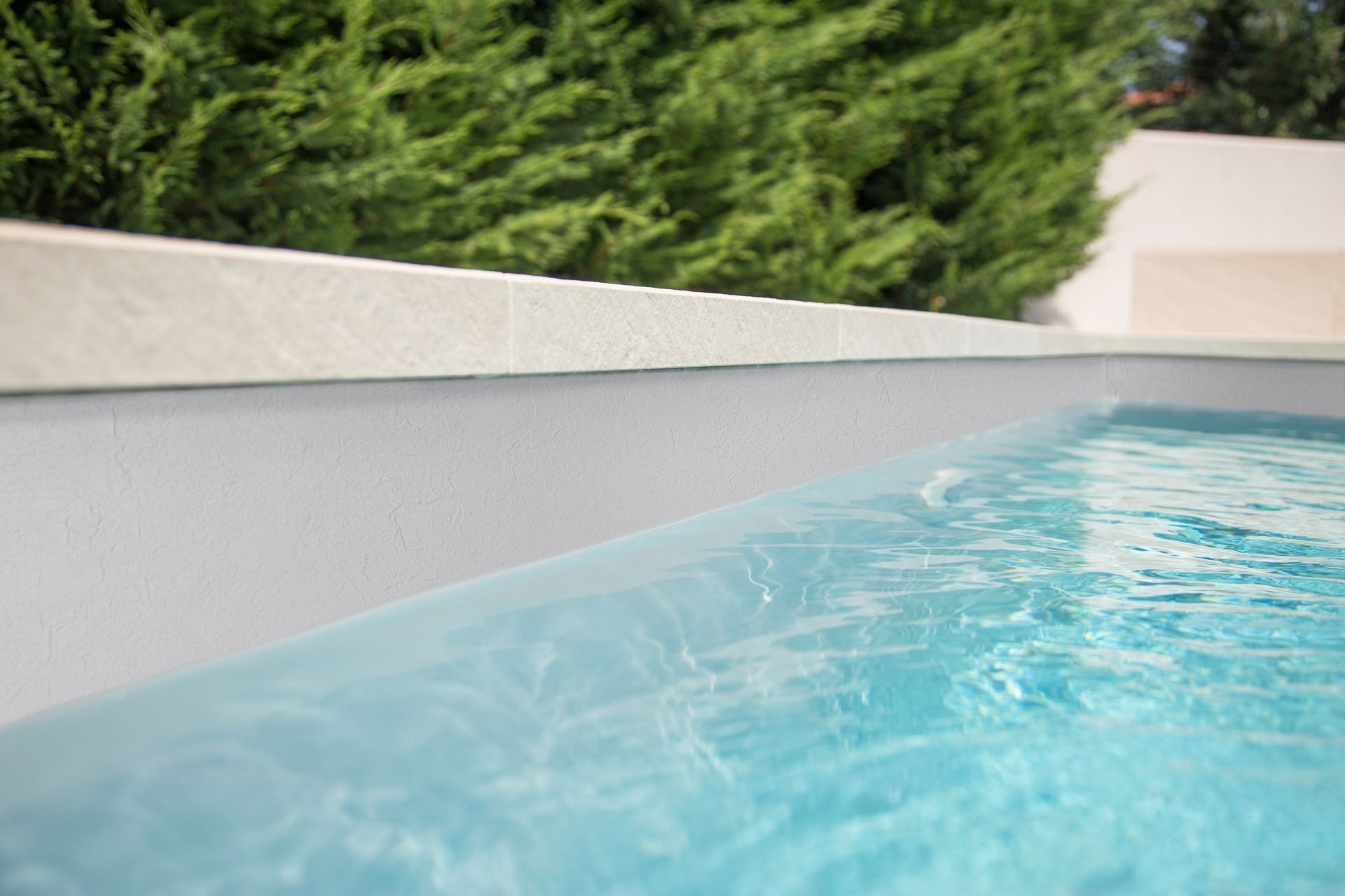 Primo piano del bordo di una piscina, dell'acqua e di un bordo in pietra su uno sfondo di fogliame verde.
