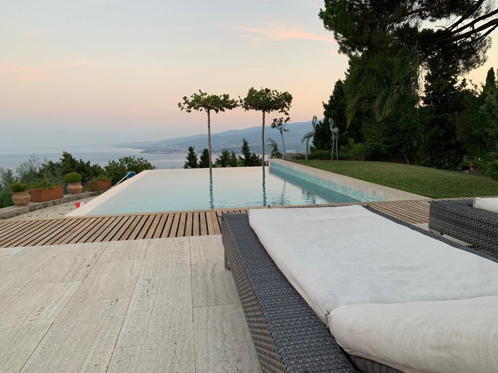 Una piscina a sfioro con vista su uno specchio d'acqua e montagne sullo sfondo al tramonto.