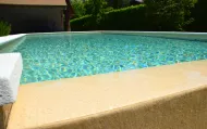 Piscina con acqua turchese e bordo in pietra beige. Posizione esterna soleggiata.