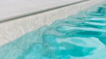 Primo piano del bordo di una piscina, acqua turchese e trasparente e cemento chiaro.