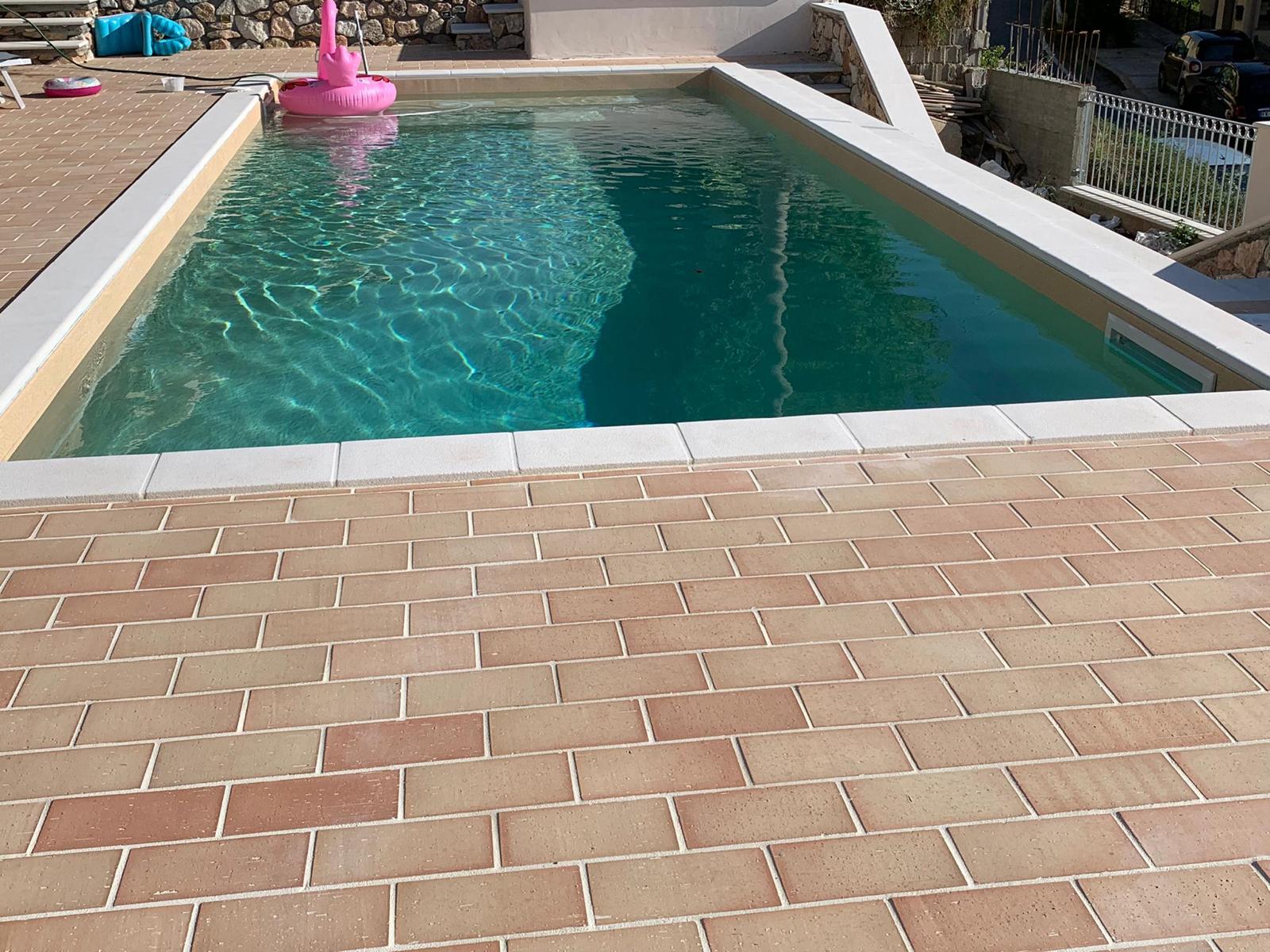 Patio in mattoni accanto a una piscina rettangolare con acqua turchese.