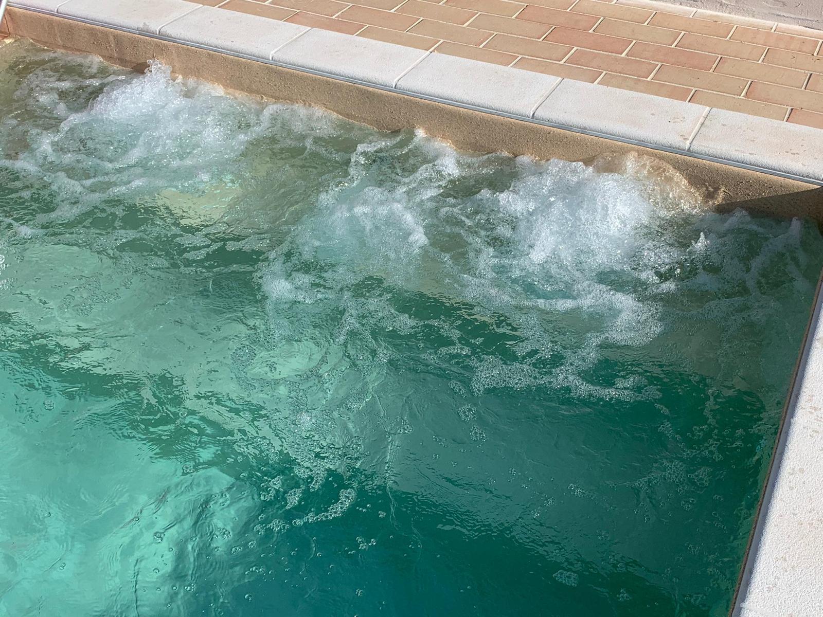 Acqua che gorgoglia in una vasca idromassaggio turchese, bordata da piastrelle color beige e bianco.
