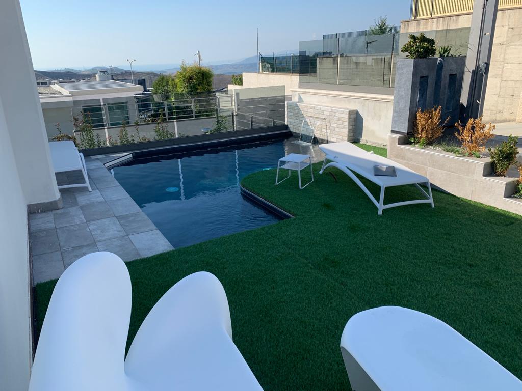 Una piscina circondata da erba sintetica e sedie a sdraio con vista sulla collina.