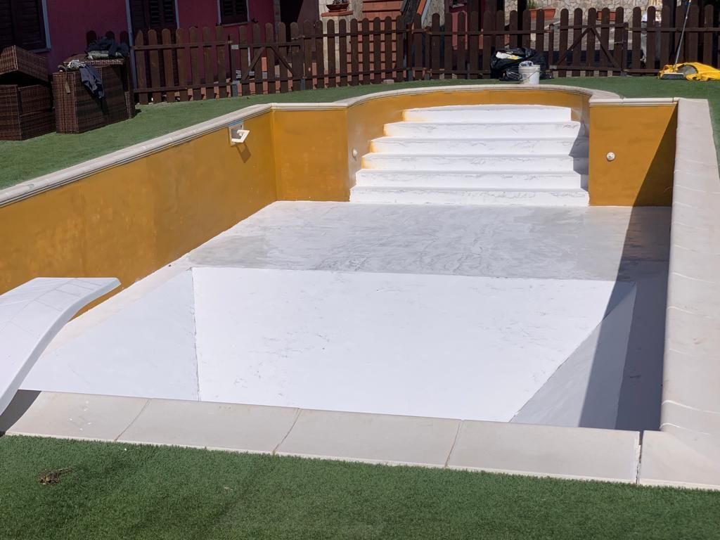 Piscina gialla e bianca con gradini e trampolino in un cortile con erba artificiale.