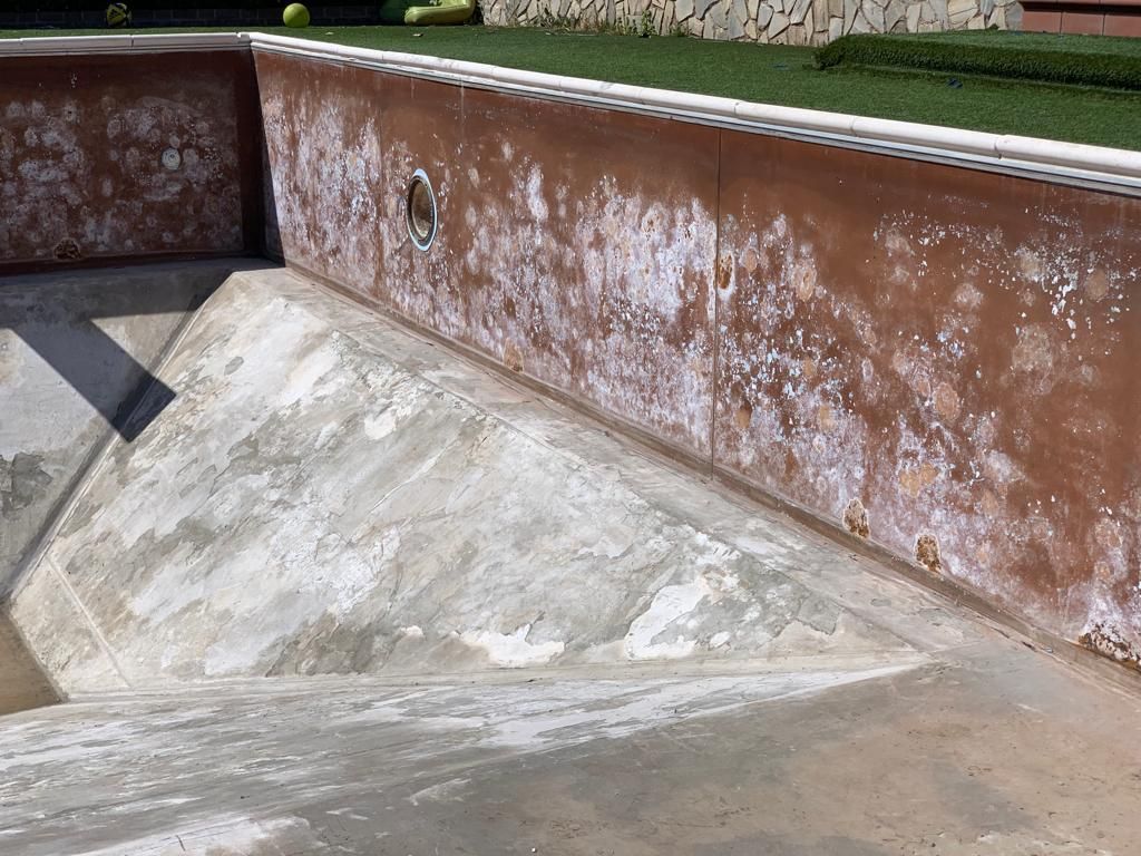 Piscina vuota in cemento con depositi minerali bianchi sulle pareti.