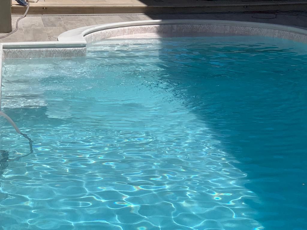 L'acqua azzurra si increspa in una piscina illuminata dal sole, con gradini e una ringhiera bianca.