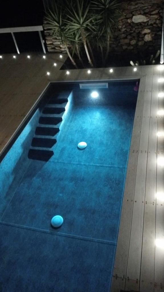 Vista notturna di una piscina con luci subacquee, gradini e luci sul ponte.