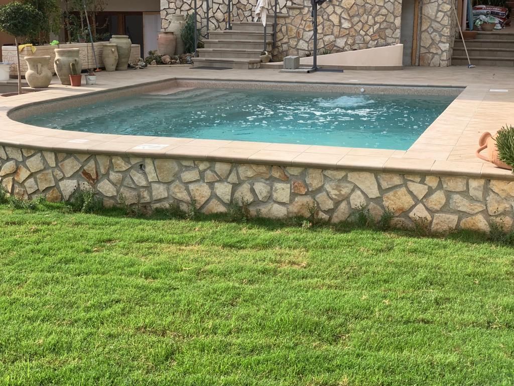 Piscina con muro in pietra e prato verde.