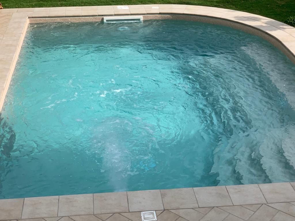 Piscina con acqua azzurra, fontane e bordo in pietra.