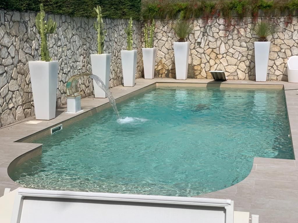 Una grande piscina circondata da piante in vaso e un muro in pietra