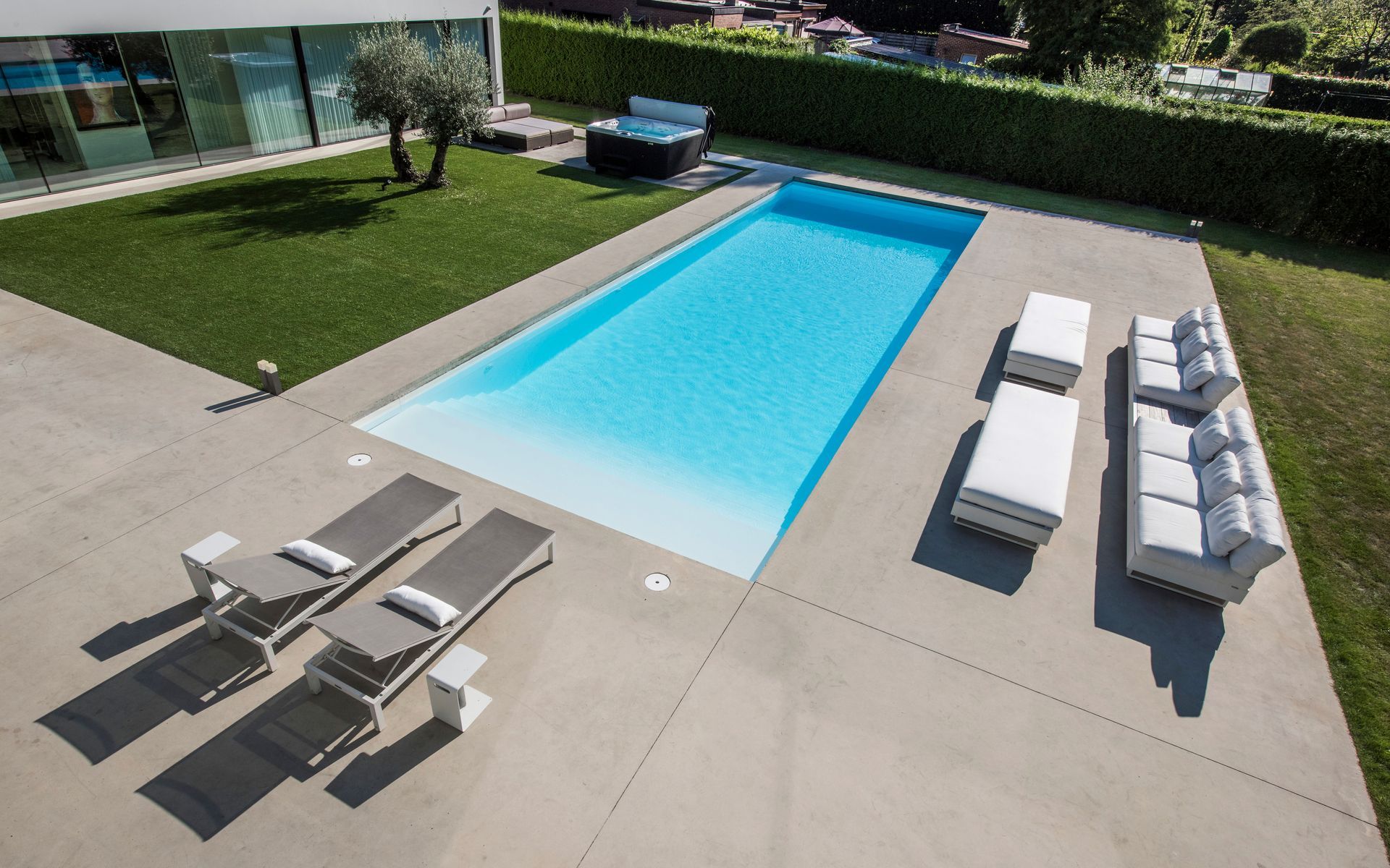 Piscina rettangolare circondata da un patio in cemento con sedie a sdraio e posti a sedere all'aperto.