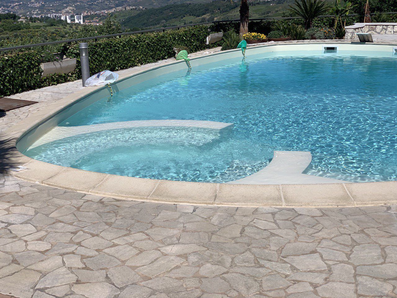 Piscina esterna con gradini e bordi in pietra, immersa nel verde.