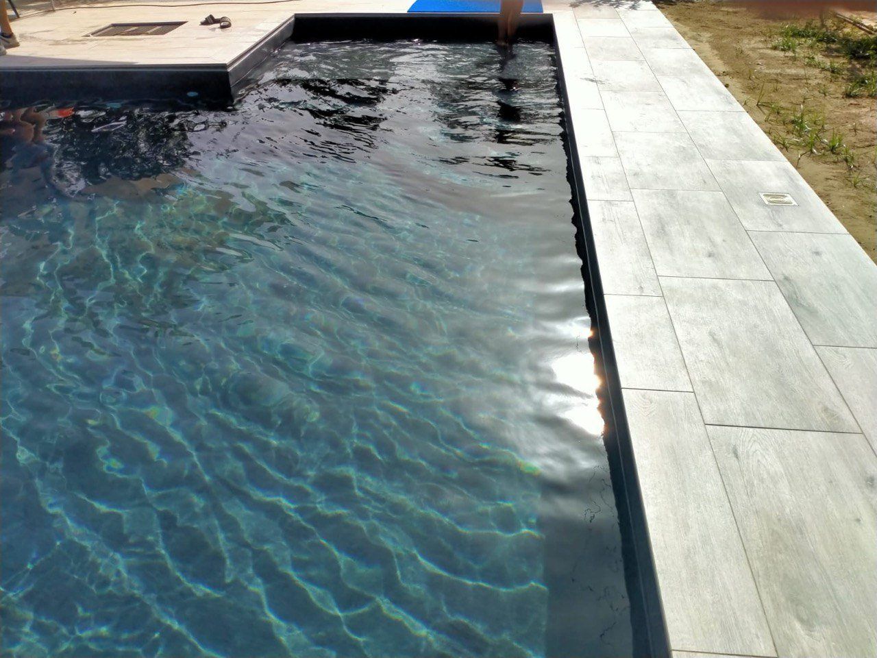 Piscina con acqua scura e bordo in pietra chiara. Le increspature sulla superficie riflettono la luce del sole.