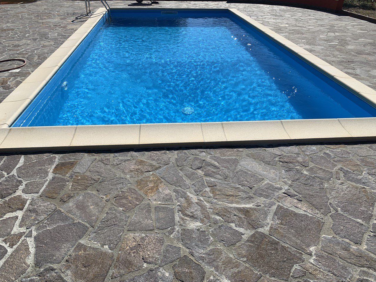 Piscina rettangolare con acqua blu circondata da piastrelle in pietra.