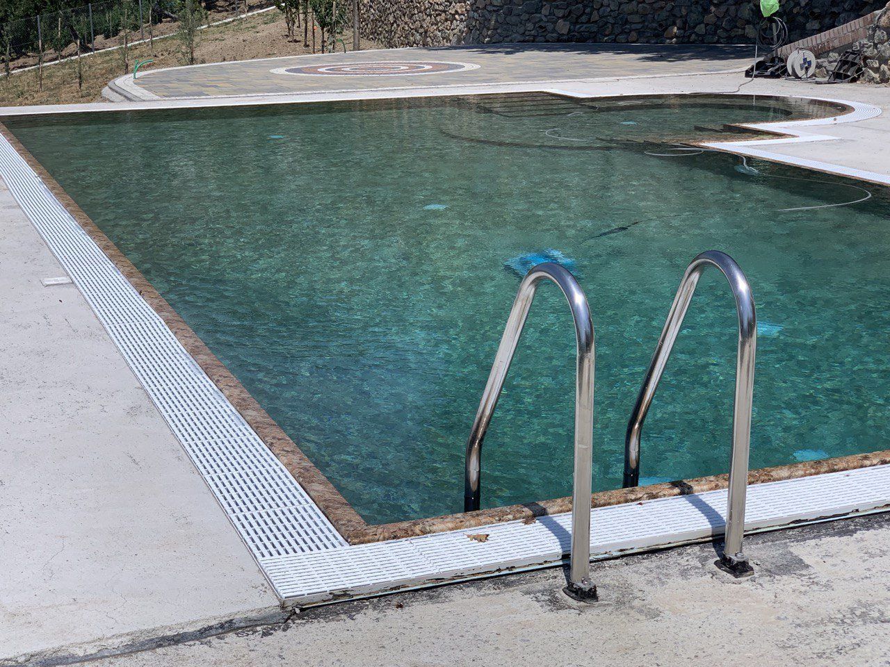 Piscina con scaletta, bordo in pietra e acqua limpida.