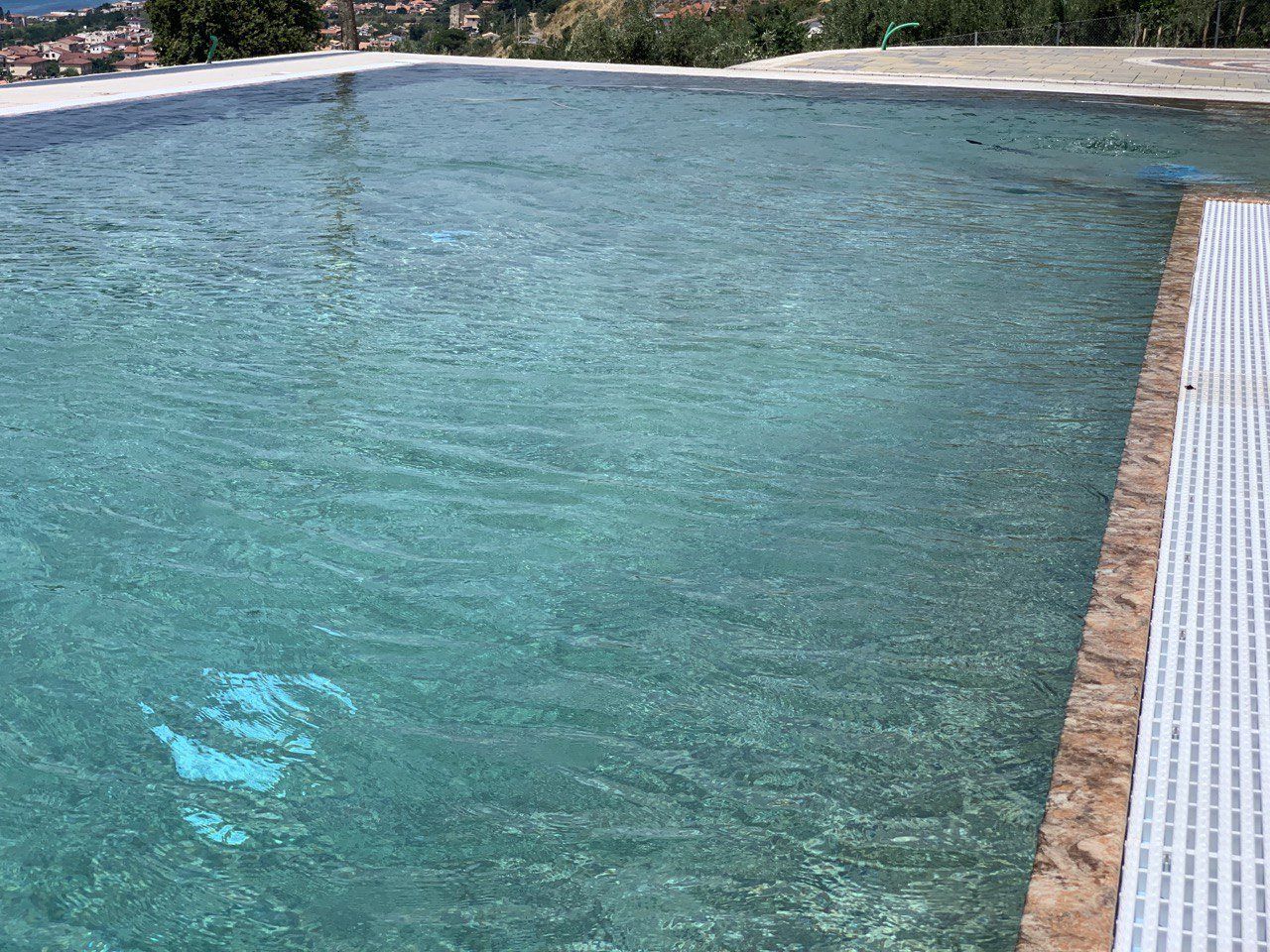 Piscina con acqua limpida e turchese. Il bordo è in pietra e il deck è in listelli bianchi. Le colline sullo sfondo.