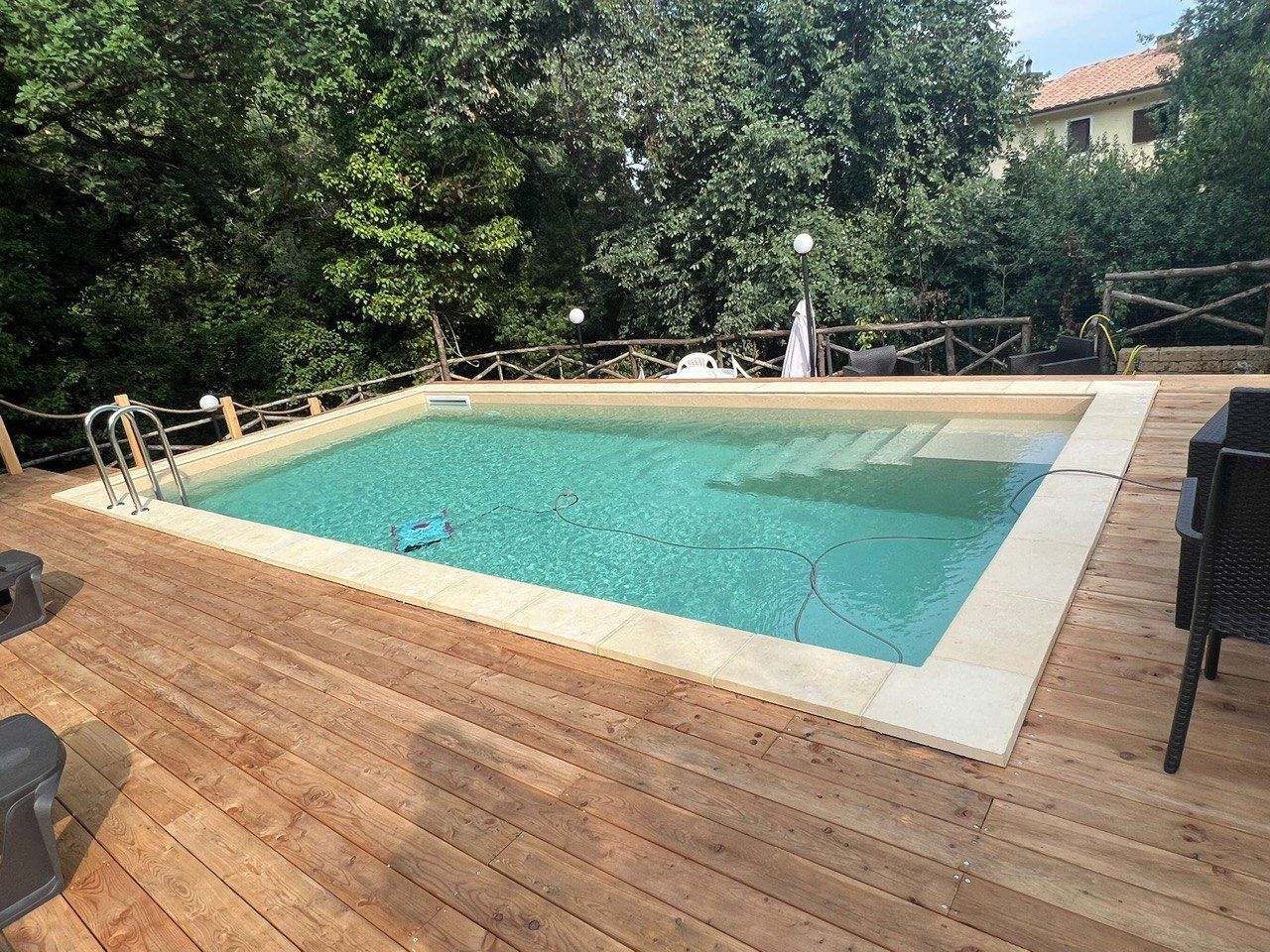Piscina circondata da un ponte in legno. Alberi verdi sullo sfondo, giornata di sole.