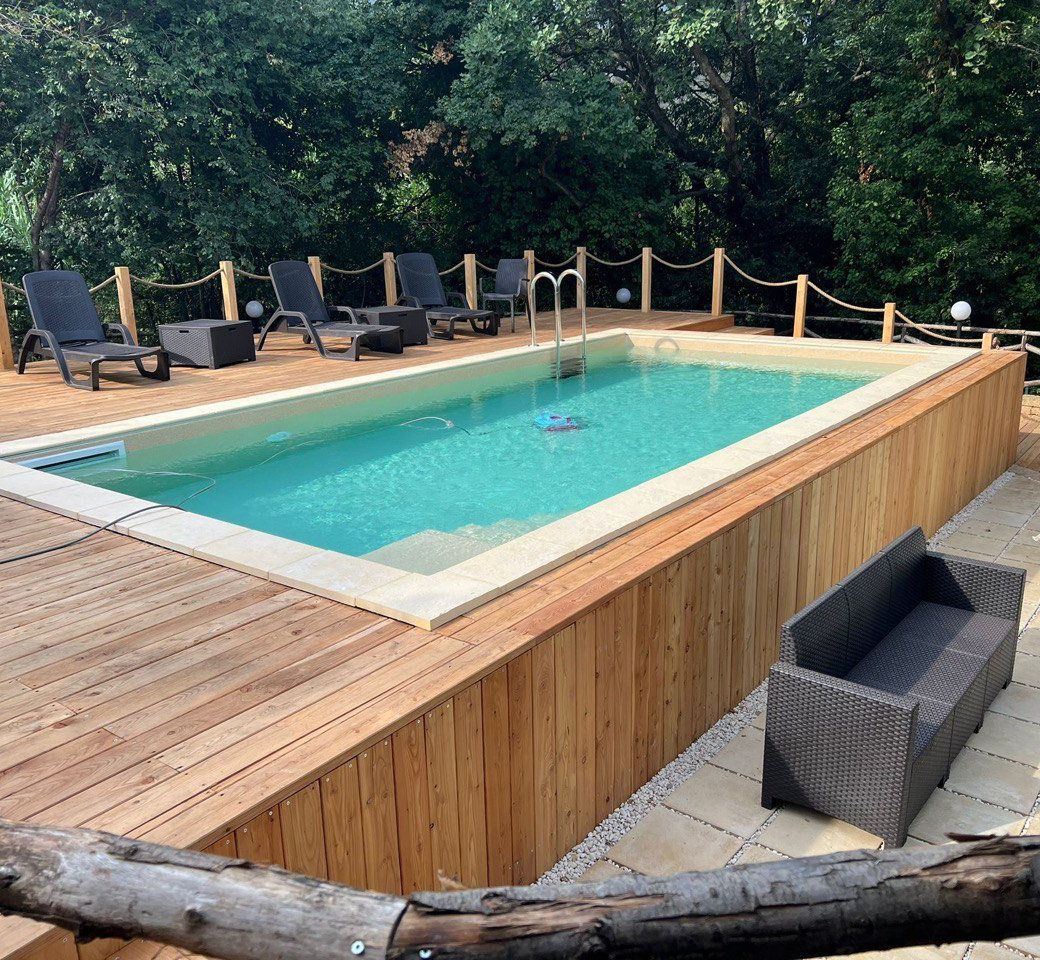 Piscina rettangolare con acqua turchese, terrazza in legno, sedie a sdraio e rigogliosi alberi verdi.
