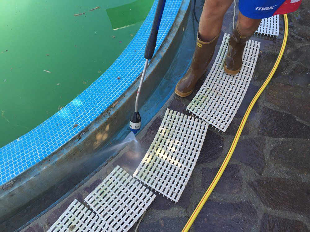 Persona che pulisce il bordo di una piscina con un'idropulitrice.