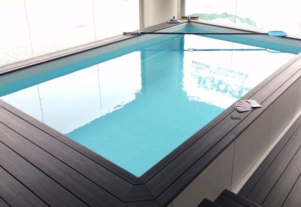 Piscina interna rettangolare con pavimentazione in legno nero e acqua turchese.