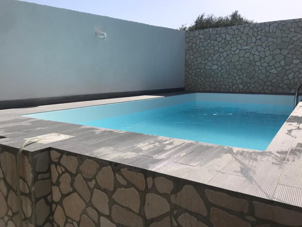Piscina rettangolare riempita di acqua blu circondata da pareti in pietra e bianche.