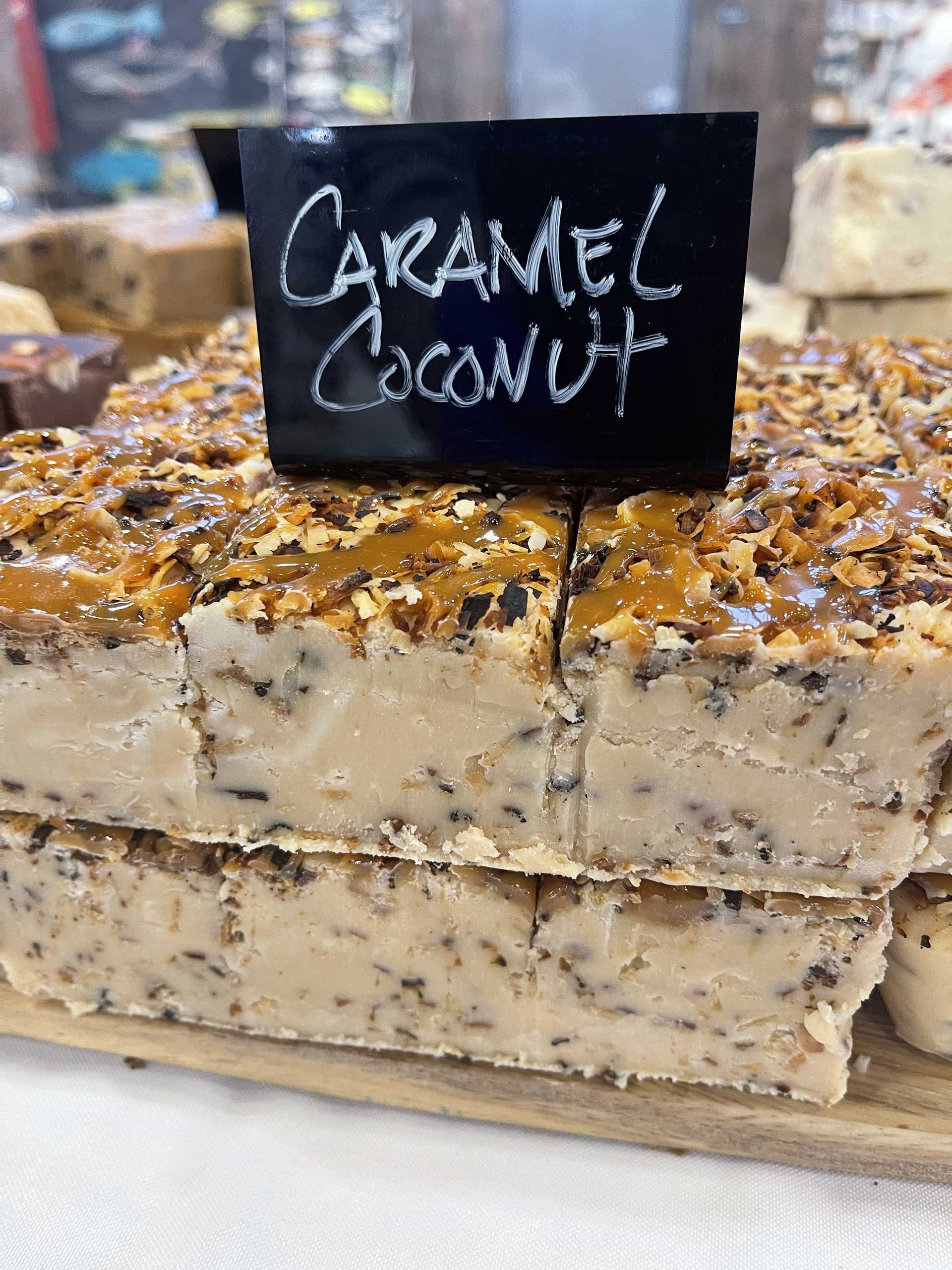 Caramel coconut fudge squares with caramel topping, on a wooden board, with a black sign.