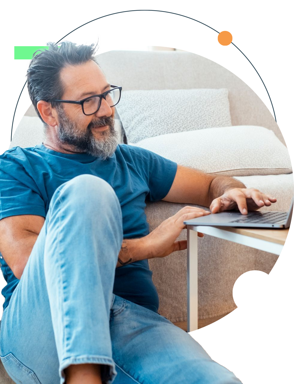 Man with glasses working on laptop while sitting near couch.