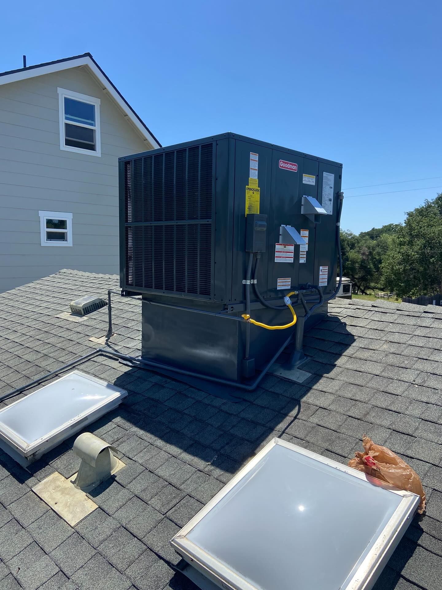 Rooftop HVAC unit beside a house, with two skylights and a blue sky overhead.