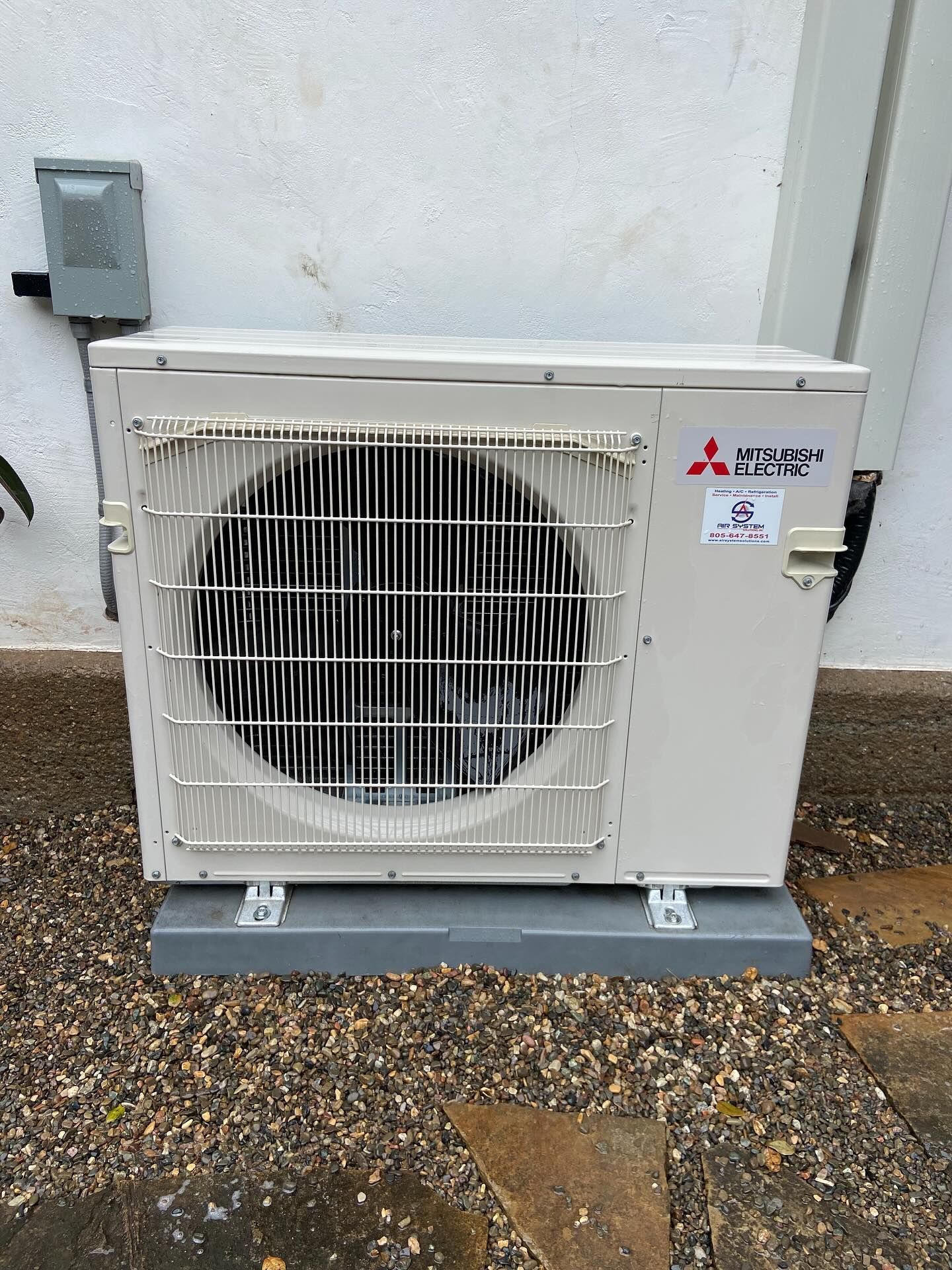 Outdoor Mitsubishi AC unit on a concrete pad beside a building wall.